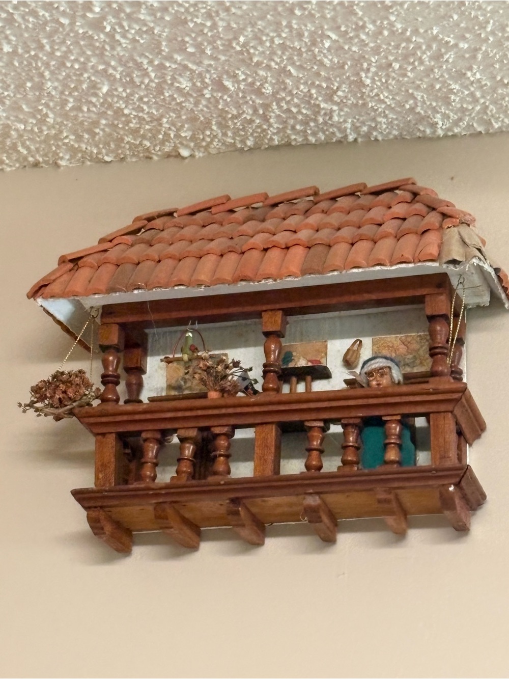 Handmade wooden balcony with miniature furniture, flora, and a seated figure